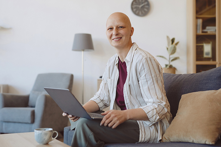 Bald woman with laptop re study on cancer therapies during COVID-19